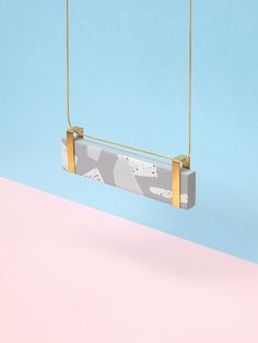 a white and grey object hanging from a gold chain on a pink and blue background