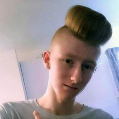 a young man with a messy topknott giving the thumbs up sign while standing in front of a mirror