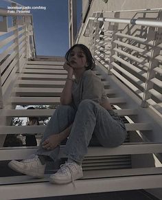 a woman sitting on top of a set of stairs next to a building with her hand under her chin