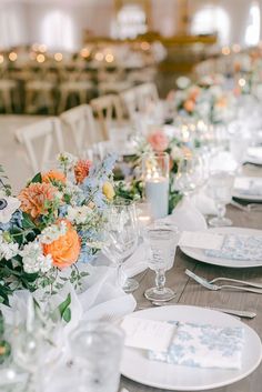 a long table is set with white and orange flowers, silverware, and place settings