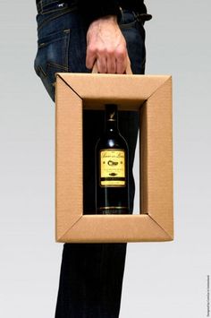 a man holding a bottle of liquor in a cardboard box that is open to reveal the contents