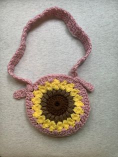 a crocheted pink and yellow purse with a brown center sits on a white surface