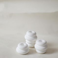 three white vases sitting on top of a white table next to eachother