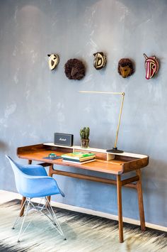 a desk with a blue chair in front of it and three masks on the wall behind it