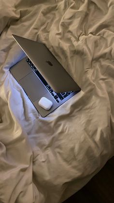 an open laptop computer sitting on top of a white bed cover covered in sheets and pillows