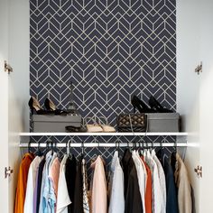 an organized closet with clothes and shoes hanging on the rack, next to a patterned wallpaper