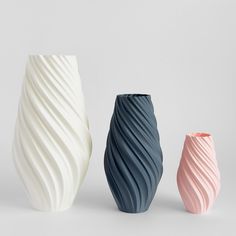 three different colored vases sitting side by side on a white surface, one is pink and the other is blue