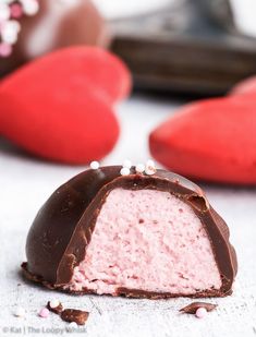 a piece of chocolate covered strawberry truffle on a white surface with pink and red heart shaped cookies in the background