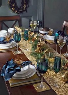 the table is set for christmas dinner with blue and gold decorations on it, along with wine glasses