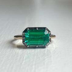 The Georgian-Victorian Emerald Cut Emerald & Blackened Gold East West Button Back Collet Ring—a timeless engagement piece inspired by the grace of the Georgian and Victorian periods. This ring, featuring a stunning 3 ct lab-grown emerald in a Georgian cut-down collet setting and button back, exudes a timeless yet modern charm. It's not just an engagement ring; it's a versatile piece designed for stacking and layering with other styles. Lab Grown Gems: Our lab grown stones are not synthetic, or t Timeless Emerald Gemstone Wedding Ring, Classic May Birthstone Jewelry For Proposal, Classic White Gold Emerald Ring For Proposal, Classic Emerald Cut Jewelry For Proposal, Classic Platinum Emerald Ring, Classic Emerald Ring With Center Stone For Proposal, Timeless Emerald Ring With Prong Setting, Formal Emerald Cut Emerald Ring With Rose Cut Diamonds, Formal Emerald Cut Ring With Rose Cut Diamonds