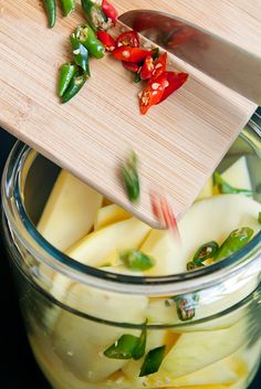 a wooden cutting board sitting on top of a glass jar filled with sliced apples and peppers