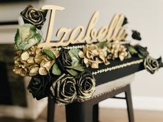 there is a cake decorated with flowers on top of a stool and name spelled in gold letters