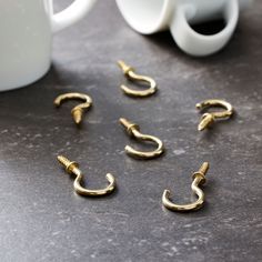 several gold - plated metal hooks are sitting on a table next to a coffee mug