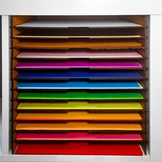 a stack of colorful folders sitting on top of a metal shelf in front of a white wall