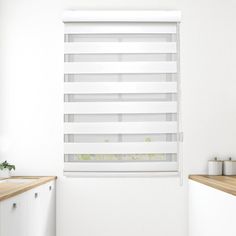 a kitchen with white walls and wooden counter tops, along with a window covered in blinds