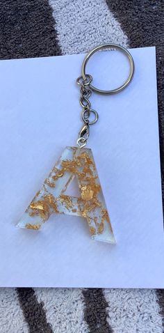 a white and gold letter shaped keychain sitting on top of a piece of paper