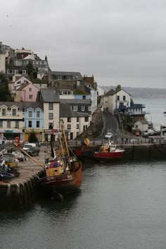 two boats are docked in the water next to some houses and buildings on the shore