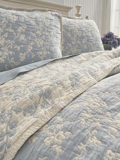 a bed with blue and white bedspread, pillows and flowers on the headboard