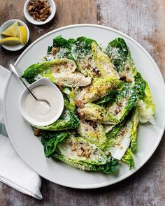 a white plate topped with lettuce covered in sauce next to bowls of dressing