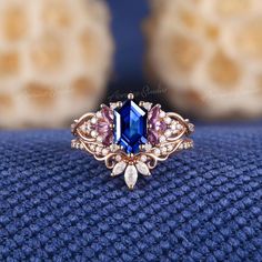 a blue ring with pink and white stones on it sitting on top of a blue cloth