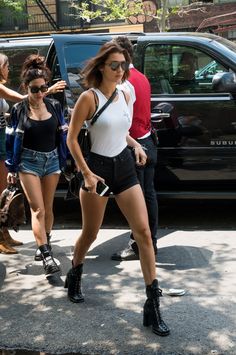 two women walking down the street in short shorts and high heeled boots, with one woman carrying a handbag