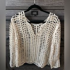 a white knitted sweater hanging on a black hanger next to a wooden wall