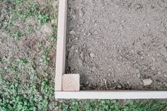 an empty wooden frame sitting in the middle of some grass and dirt with weeds growing around it