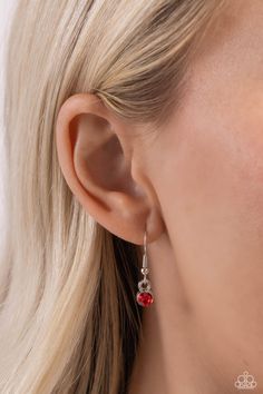 a woman with blonde hair wearing a pair of red and silver earrings on her left ear