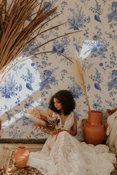 a woman sitting on the floor reading a book next to some vases and plants