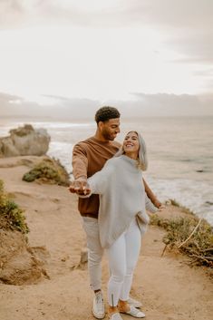 a man and woman are walking along the beach holding each other's hands as they smile