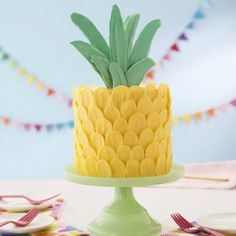 a yellow pineapple cake on a green pedestal with forks and napkins around it