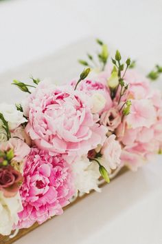 pink and white flowers are arranged in a wooden box on a table with greenery