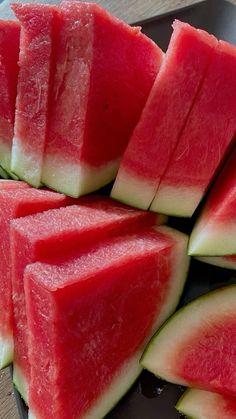 slices of watermelon are arranged on a black plate with a silver serving spoon