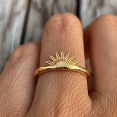 a woman's hand wearing a gold ring with the sun on it