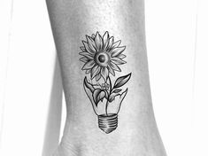 a black and white photo of a sunflower with a lightbulb tattoo on the ankle