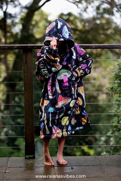 Girl wearing a vibrant colored mushroom print roomy hooded blanket. The mushrooms are psychedelic inspired, different designs and colors.