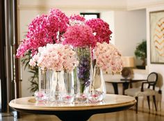 pink and white flowers are in clear vases on a round table with black legs