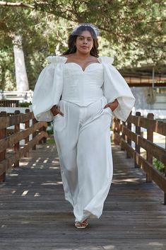 a woman in white is walking down a wooden walkway with her hands on her hips