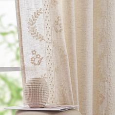 a white vase sitting on top of a chair next to a window with curtains behind it