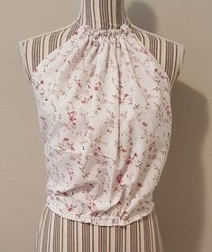 "I made this gorgeous bohemian style halter top repurposing linens, by pulling the neck and waist strings to tie where needed, this garment will fit from an x-small to a medium. The crocheted flower is also a pin to remove or place where desired. For a better visual, the mannequin's measurements are bust 34\"." Affordable Multicolor Bohemian Halter Top, Bohemian Sleeveless Halter Top With Floral Print, Bohemian Halter Top With Floral Print, Bohemian Sleeveless Crop Top With Floral Print, Spring Festival Sleeveless Halter Top, Bohemian Sleeveless Floral Print Crop Top, Bohemian Cropped Halter Top For Spring, Bohemian Cropped Halter Top For Vacation, Bohemian Flowy Crop Top For Spring