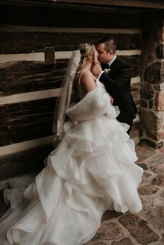 a bride and groom kissing in front of a log cabin