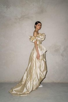 a woman in a gold dress standing against a wall