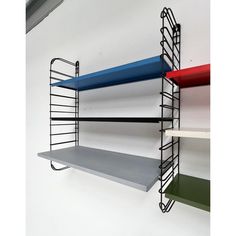 three shelves are hanging on the wall with different colors and shapes, one is empty