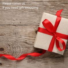 a gift wrapped in white paper with red ribbon on wooden background, saying please convo us if you need gift wrapping