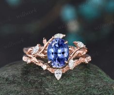 a blue sapphire and diamond ring sitting on top of a green mossy rock with leaves