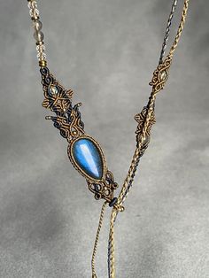 a necklace with a blue stone and gold chains on it's end, sitting on a gray surface