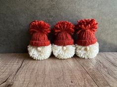 three red and white knitted santas hats sitting on top of a wooden table