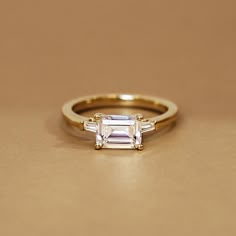 Emerald Cut East West Tapered Baguette Diamond Engagement Ring - 18K Yellow Gold. This modern ring takes a classic silhouette and elevates it with the addition of east west set tapered baguette diamonds that shine brightly, making this style the perfect choice for anyone looking for a three stone ring with a twist (1/5 total carat weight).

This Most Loved piece displays the best and brightest in fashion and design and is beloved by Brilliant Earth designers and customers alike. Earth Engagement Rings, Pretty Engagement Rings, Dream Wedding Ring, Cute Engagement Rings, Future Engagement Rings, Agate Engagement Ring, Baguette Diamond Rings, Emerald Engagement Ring Cut, Engagement Ring Diamond Cut