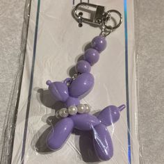 a purple dog keychain with pearls on it's collar is in the package