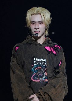 a young man with blonde hair wearing a hoodie and holding a microphone in his mouth